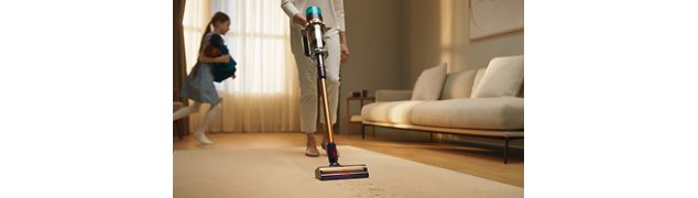 Staubsaugen im Wohnzimmer mit Kind im Hintergrund