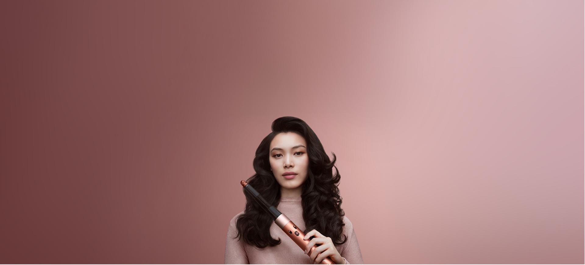 A model with brunette coily hair in a stretched blowout style holding the Dyson Airwrap i.d. multi-styler and dryer.