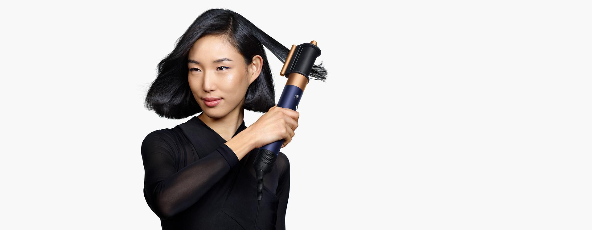 Model using the Dyson Airwrap i.d. multi-styler and dryer to style hair.