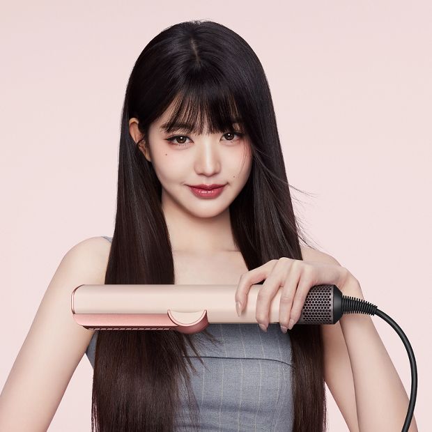 Model menghaluskan dan meluruskan rambutnya dengan pengering dan pelurus rambut Dyson Airstrait.