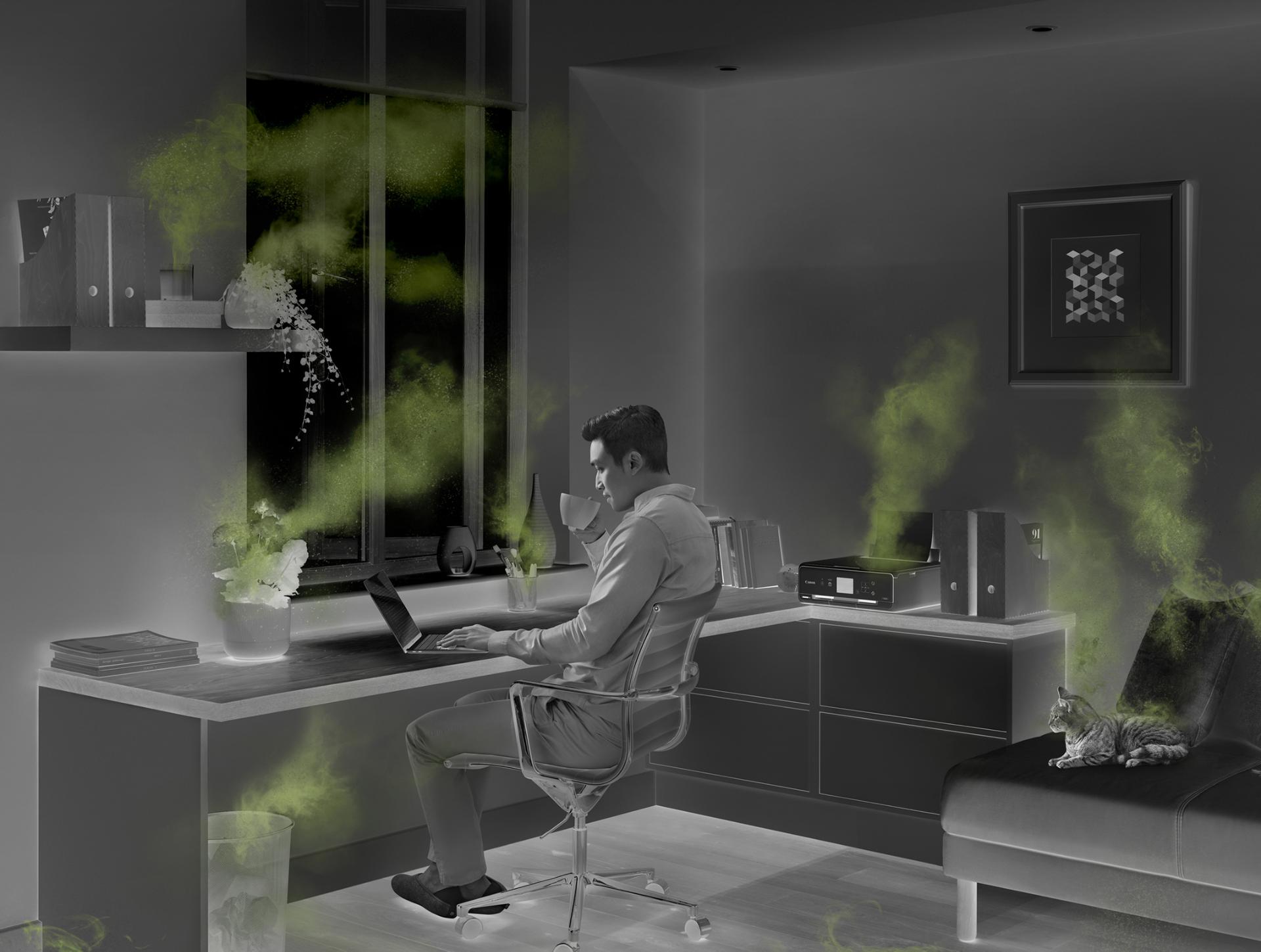 Hombre que trabaja en una oficina en casa, rodeado de fuentes de contaminación del aire interior.