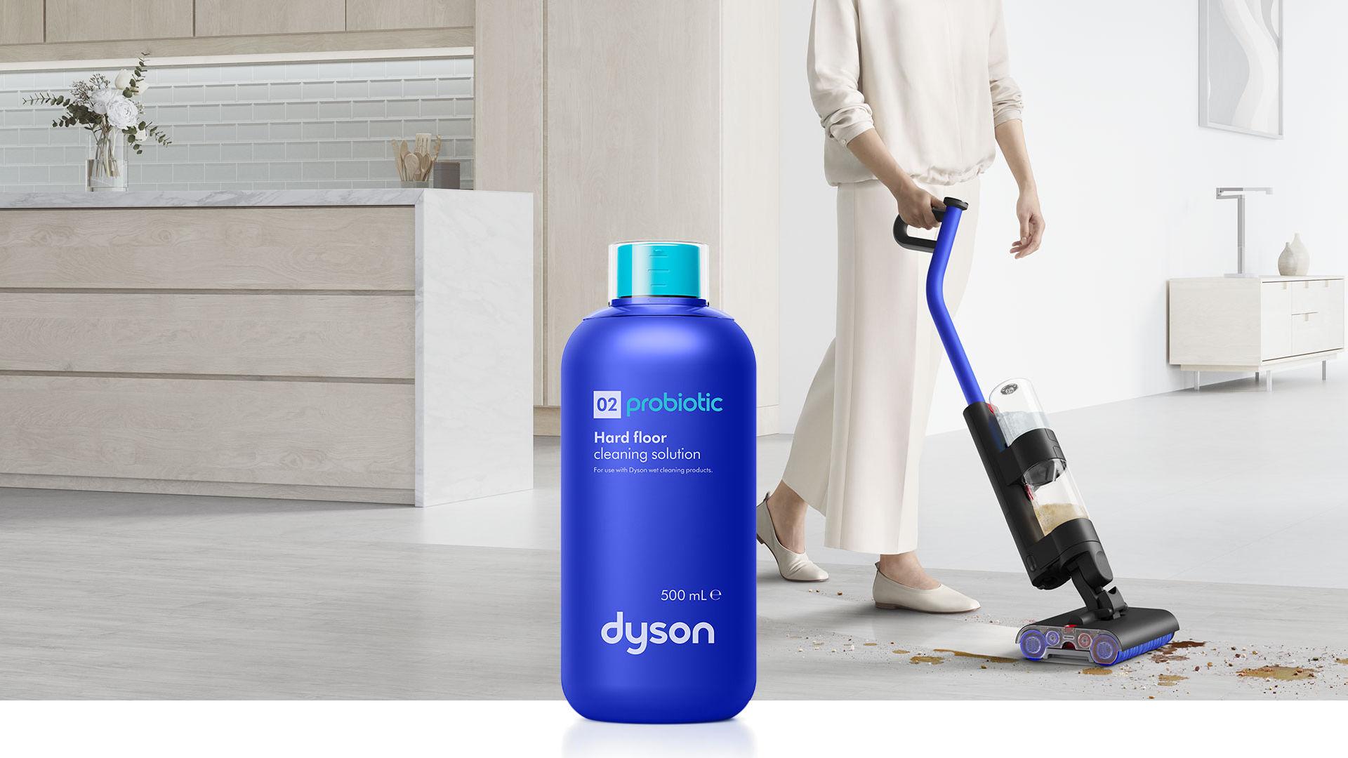 Zdjęcie przestawiające płyn do mycia podłóg Dyson 02 Probiotic na tle mopa elektrycznego Dyson WashG1 myjącego podłogę