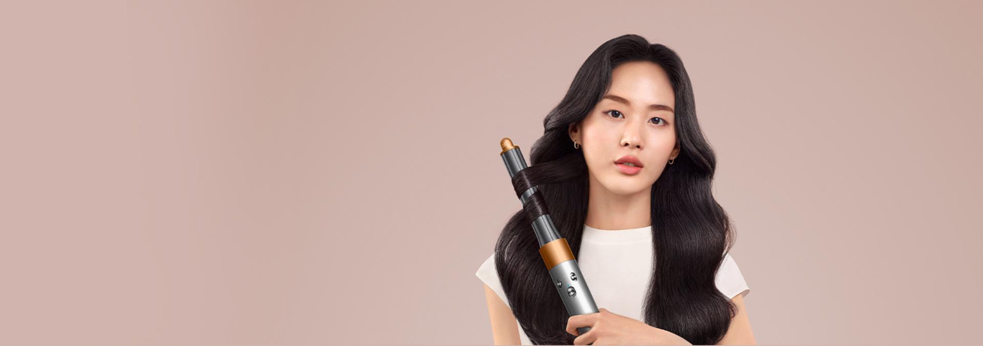 A brunette model smooths flyaways with her Dyson Airwrap Origin multi-styler and dryer.