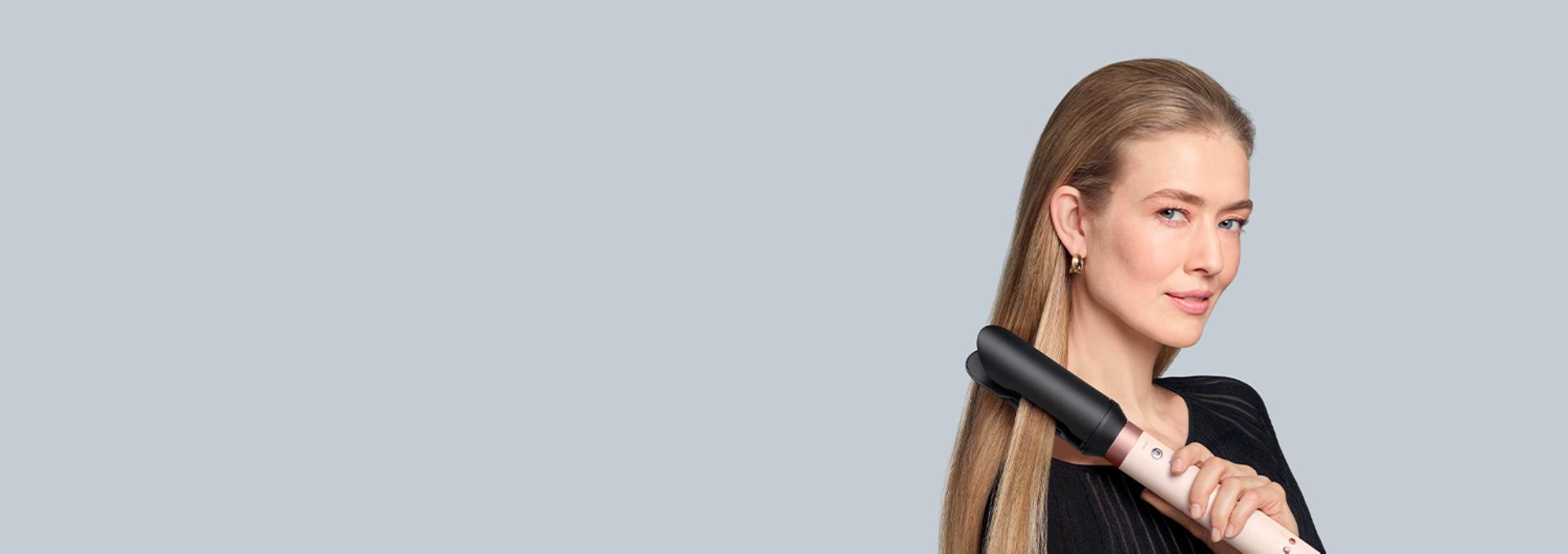 A blonde model straightens her hair using the Dyson Co-anda2x multi-styler and dryer and the AirSmooth2x attachment.