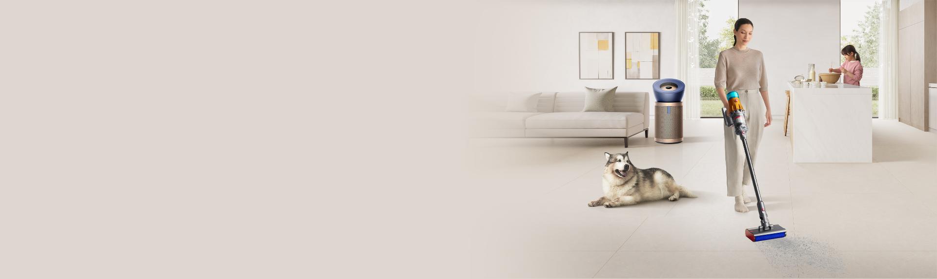 Woman vacuuming the floor with a pet dog and purifier at the background
