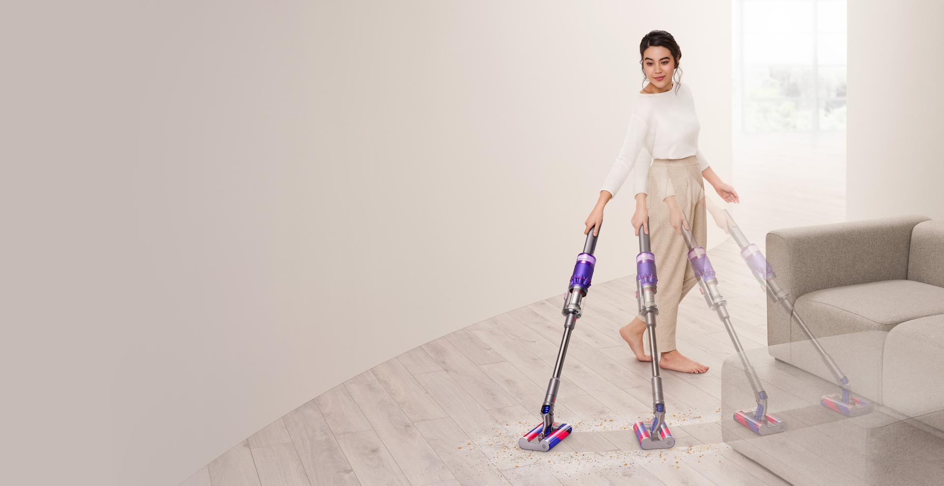 Woman vacuuming hard floor around sofa with the Dyson Omni-glide™ vacuum.