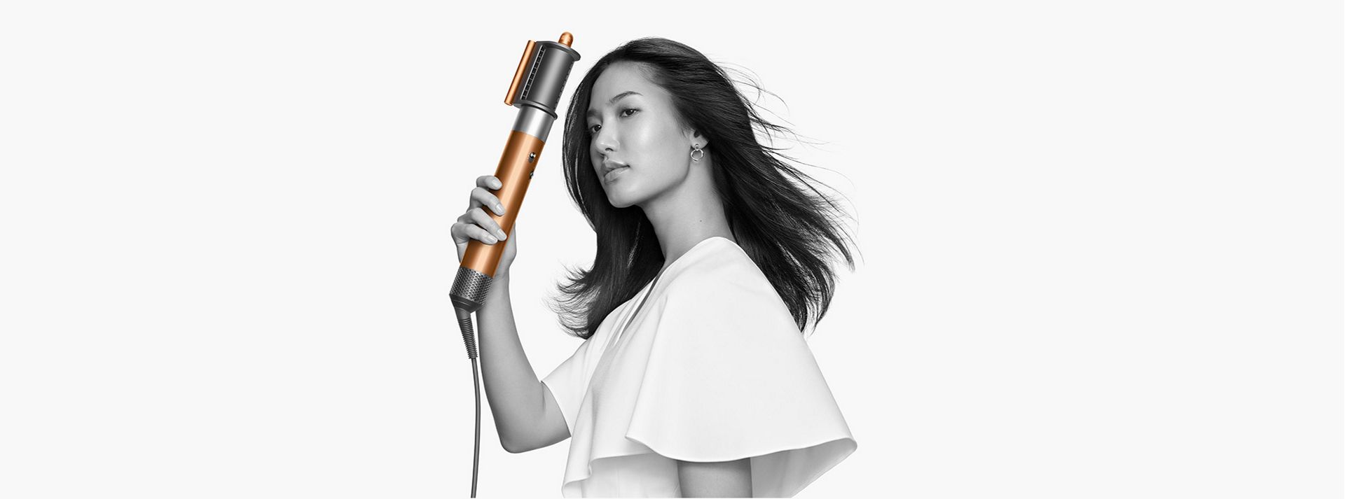 Model holding Dyson Airwrap while the fast dryer blows her hair.