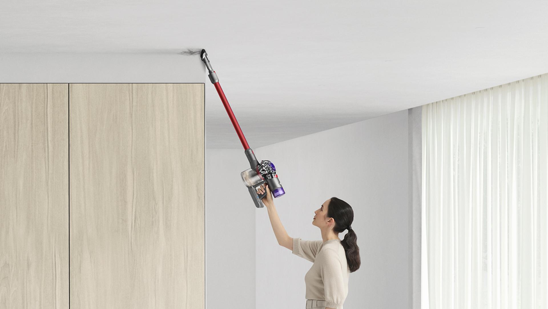 Dyson V8 kablosuz süpürge ile yüksek bir alanı temizleyen kadın