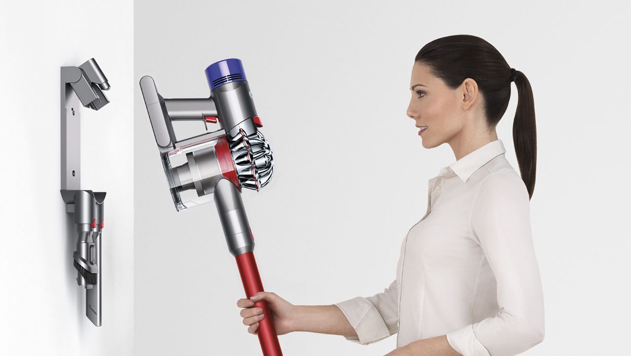 Femme rangeant l’aspirateur Dyson V8 sur sa station de charge murale