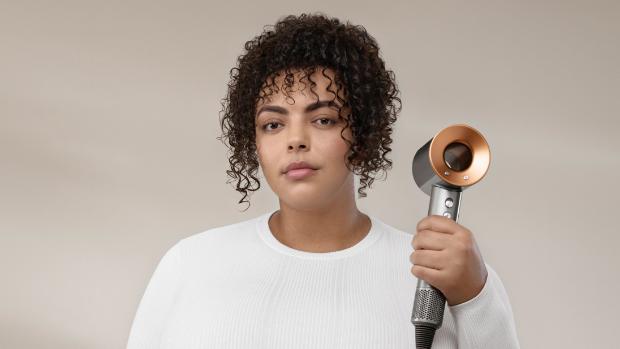 A picture of a woman with curly, brown hair, holding the Dyson Supersonic
