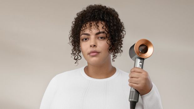 A picture of a woman with curly, brown hair, holding the Dyson Supersonic