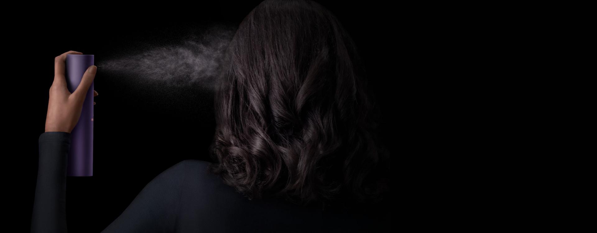 Model with dark hair applies Dyson Chitosan Multi-use styling spray to her hair.