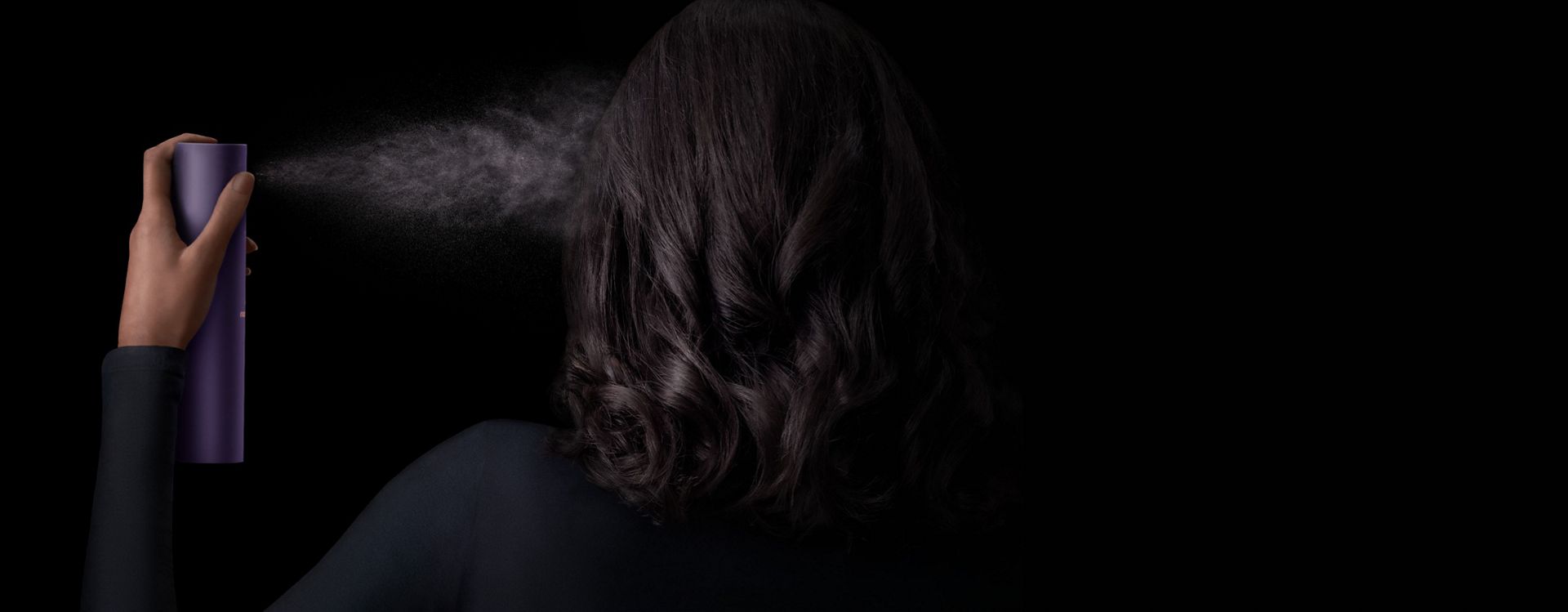 Model with dark hair applies Dyson Chitosan Multi-use styling spray to her hair.