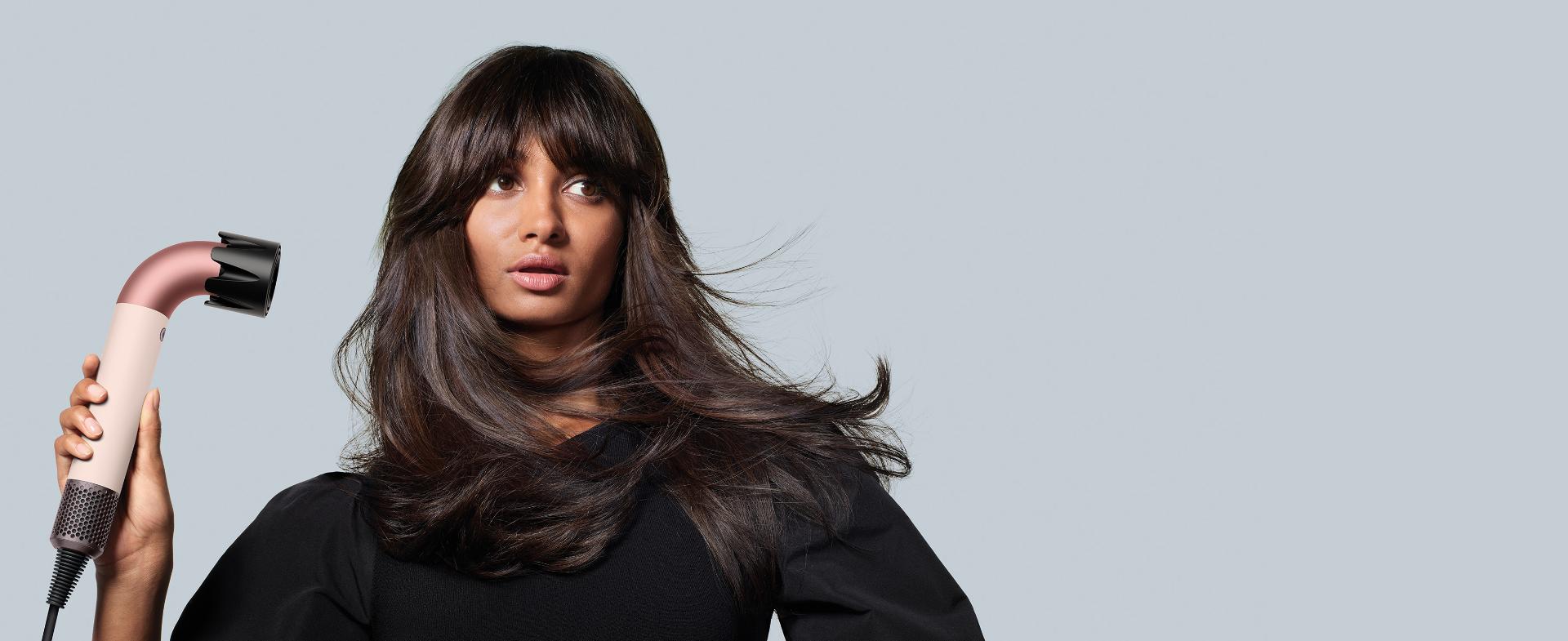 سيدة سمراء تستعمل مجفف الشعر Dyson Supersonic r لتجفيف شعرها سريعاً.