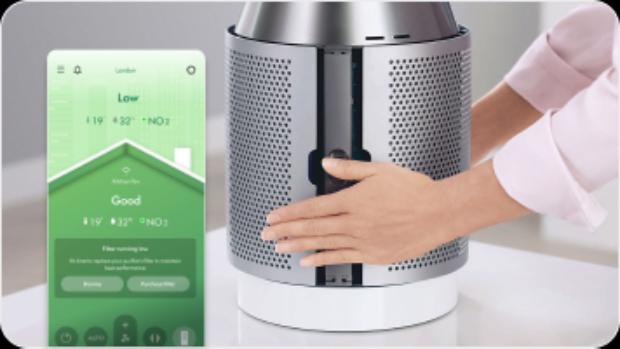 Owner fitting the filter shroud back onto their Dyson purifier with the MyDyson app reporting their air quality.
