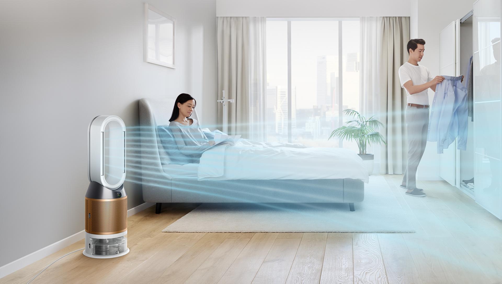 Una mujer se relaja en la cama mientras su ventilador humidificador Dyson hace circular el aire por toda la habitación