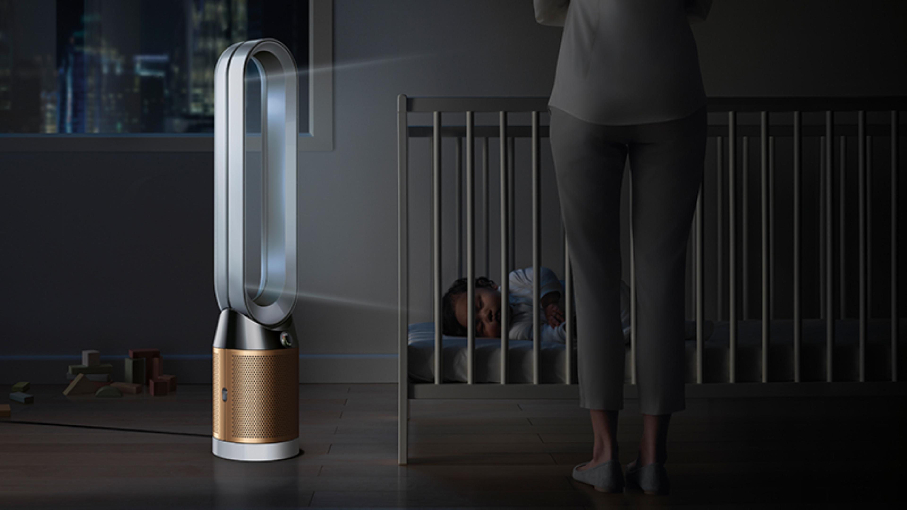 A baby sleeping soundly in their cot, while a Dyson Pure Cryptomic purifier projects purified air in Night mode