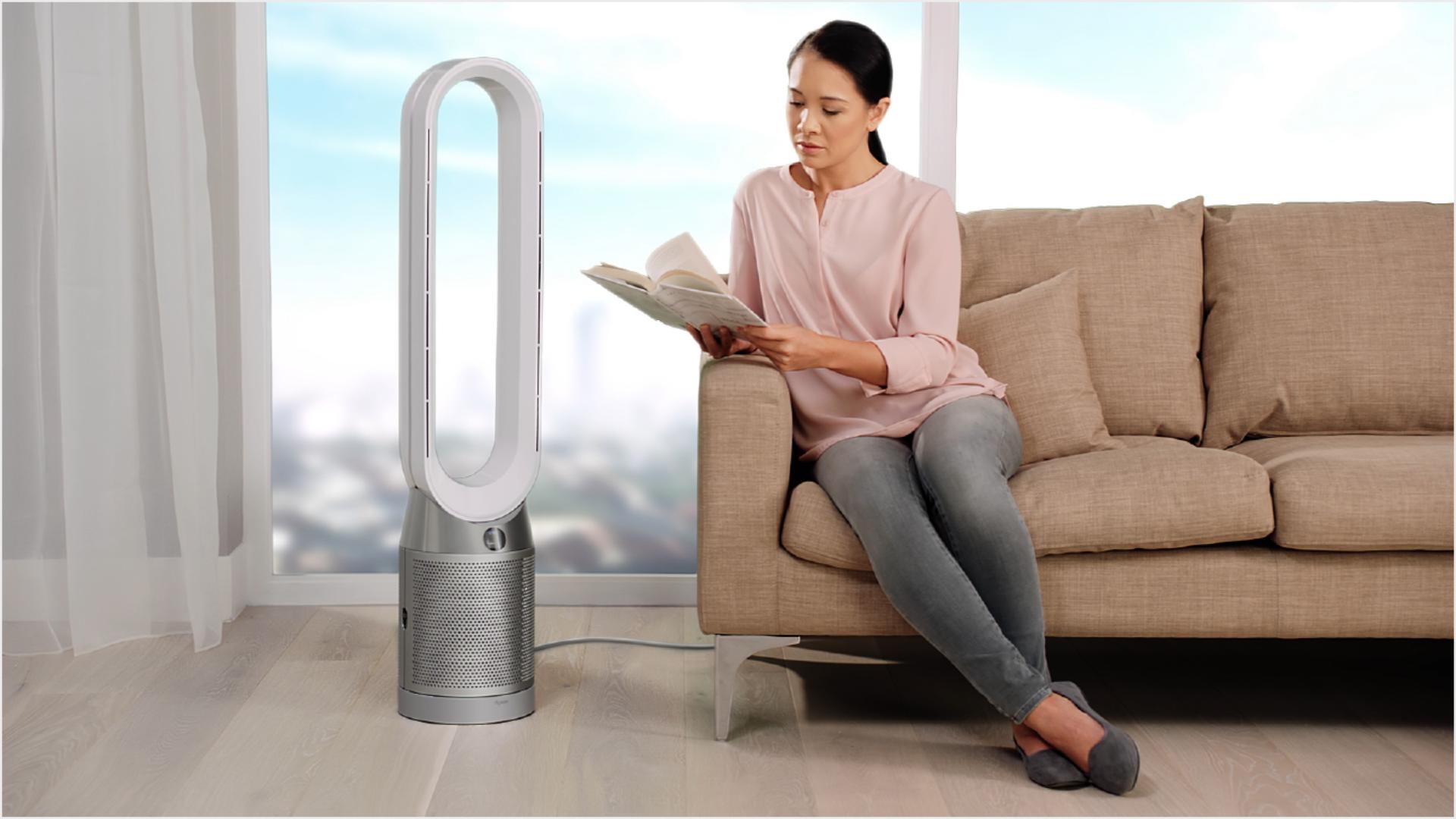 A woman on sofa adjusting the airflow of the purifier beside her.