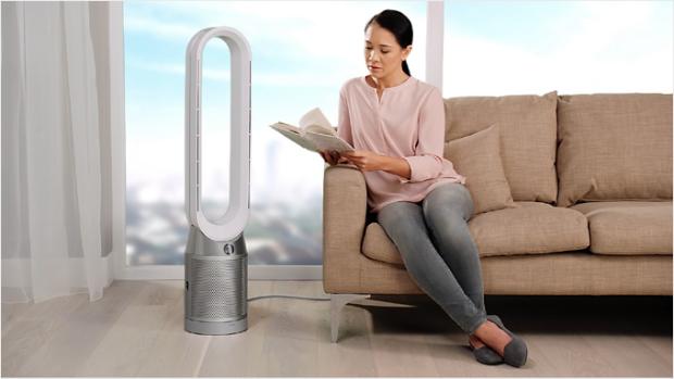 A woman on sofa adjusting the airflow of the purifier beside her.