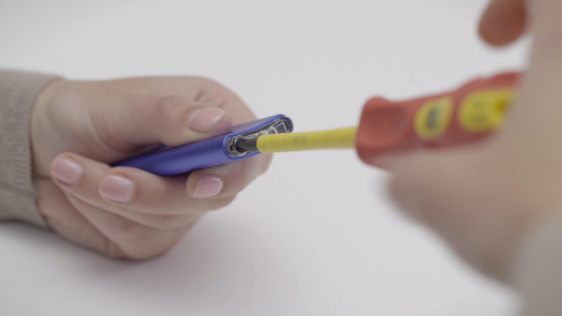 The screw on the bottom of the remote control being removed by a screw driver.