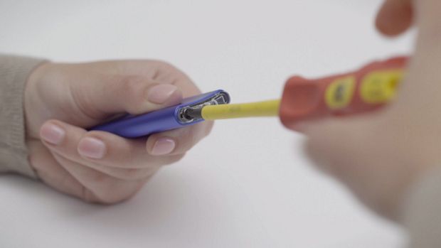 The screw on the bottom of the remote control being removed by a screw driver.
