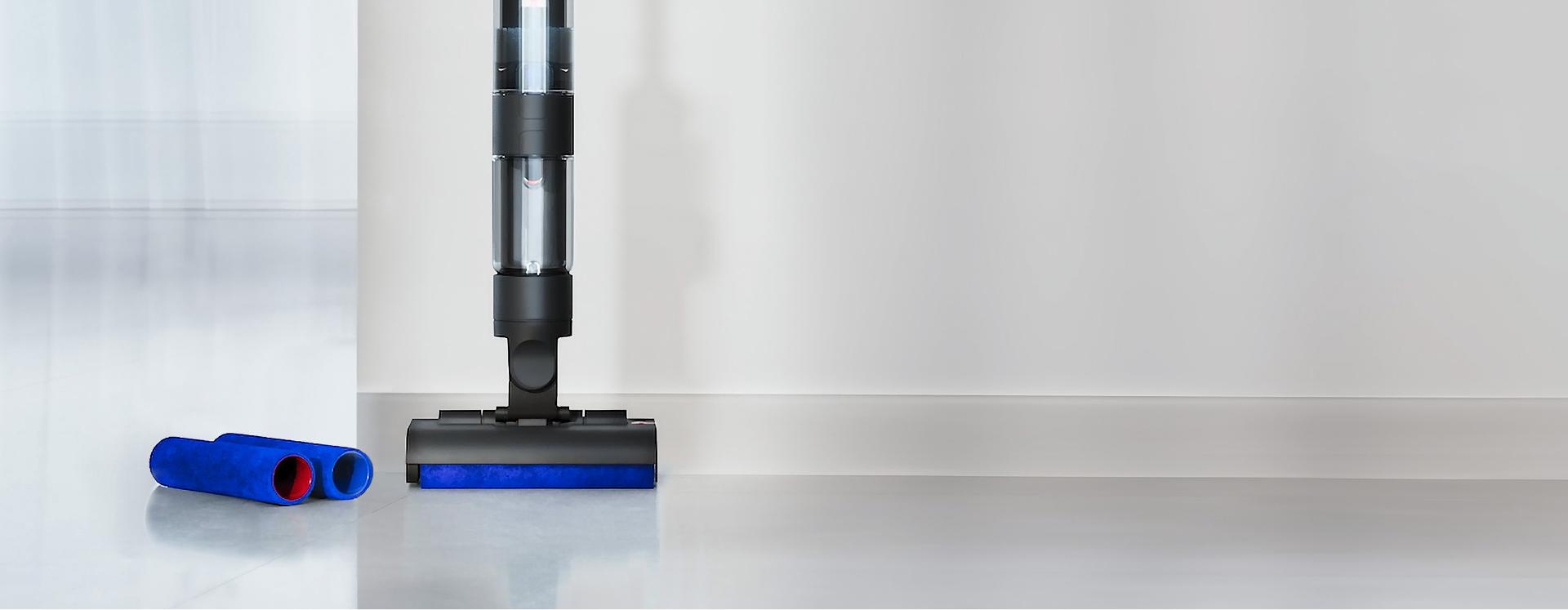 مكنسة Dyson WashG1 في وضعية واقفة على أرضية صلبة نظيفة، بجوار وحدتين أسطوانيتين من الألياف الدقيقة بديلتين