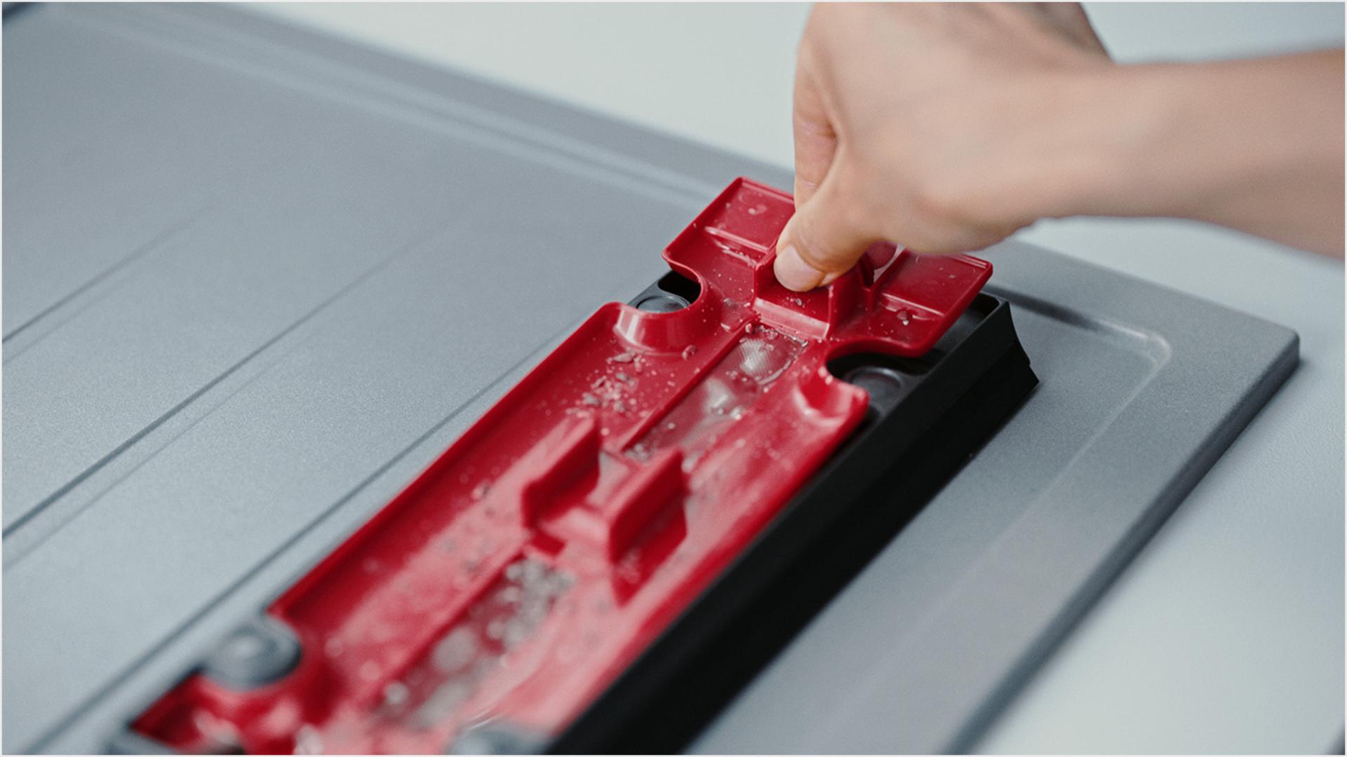 Naudotojo ranka, pakelianti raudoną vidinę dalį nuo išorinio šiukšlių dėklo korpuso