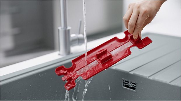A user rinsing the red inner section under a running tap