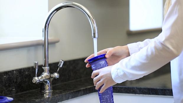 Osoba čisti filtar uređaja Dyson za automobil + čamac pod tekućom vodom iz slavine.