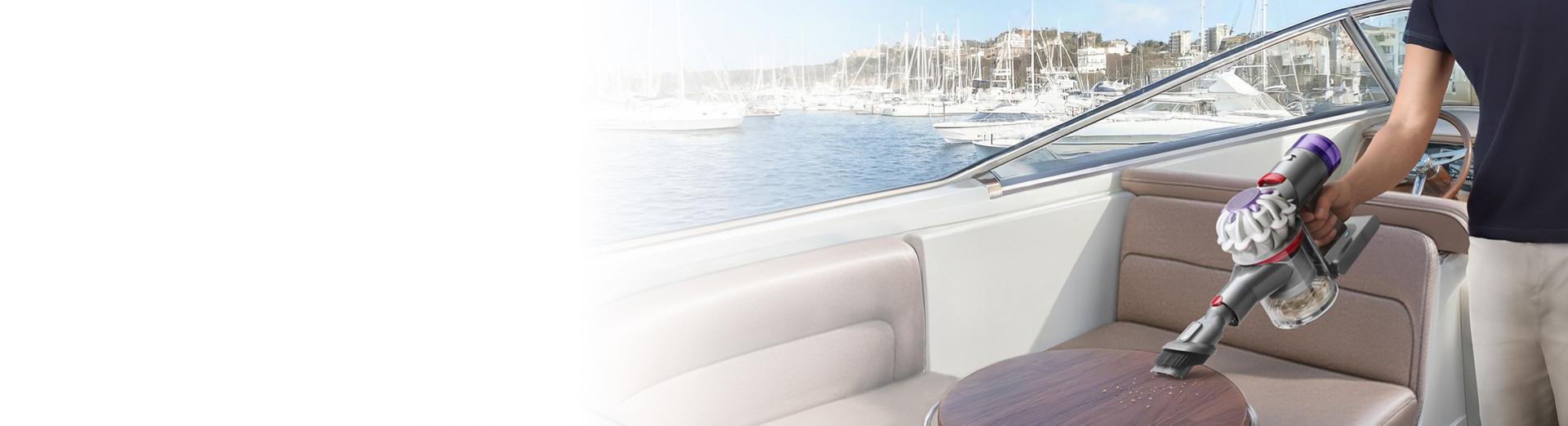 A Dyson Car+Boat handheld vacuum with the Combination tool cleans debris from a table.