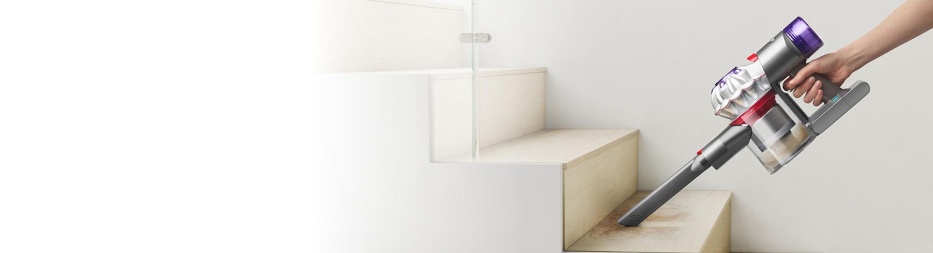 A Dyson Car+Boat handheld vacuum with the Crevice tool cleans into the corner of stairs.