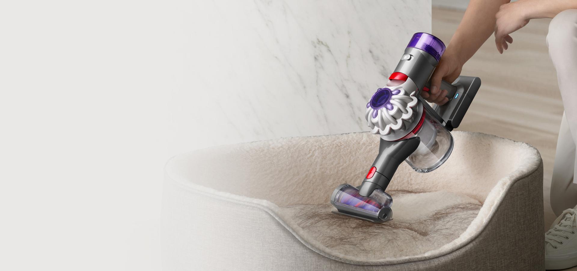 User cleaning hair from a dog bed, with the Dyson V8 Focus handheld Hair screw tool attachment.
