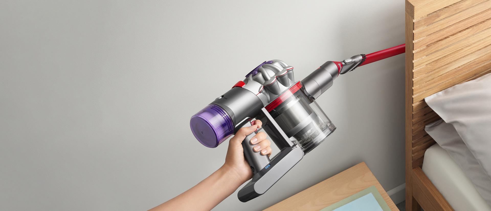 User cleaning behind a bed headboard, with the Awkward gap tool attachment.