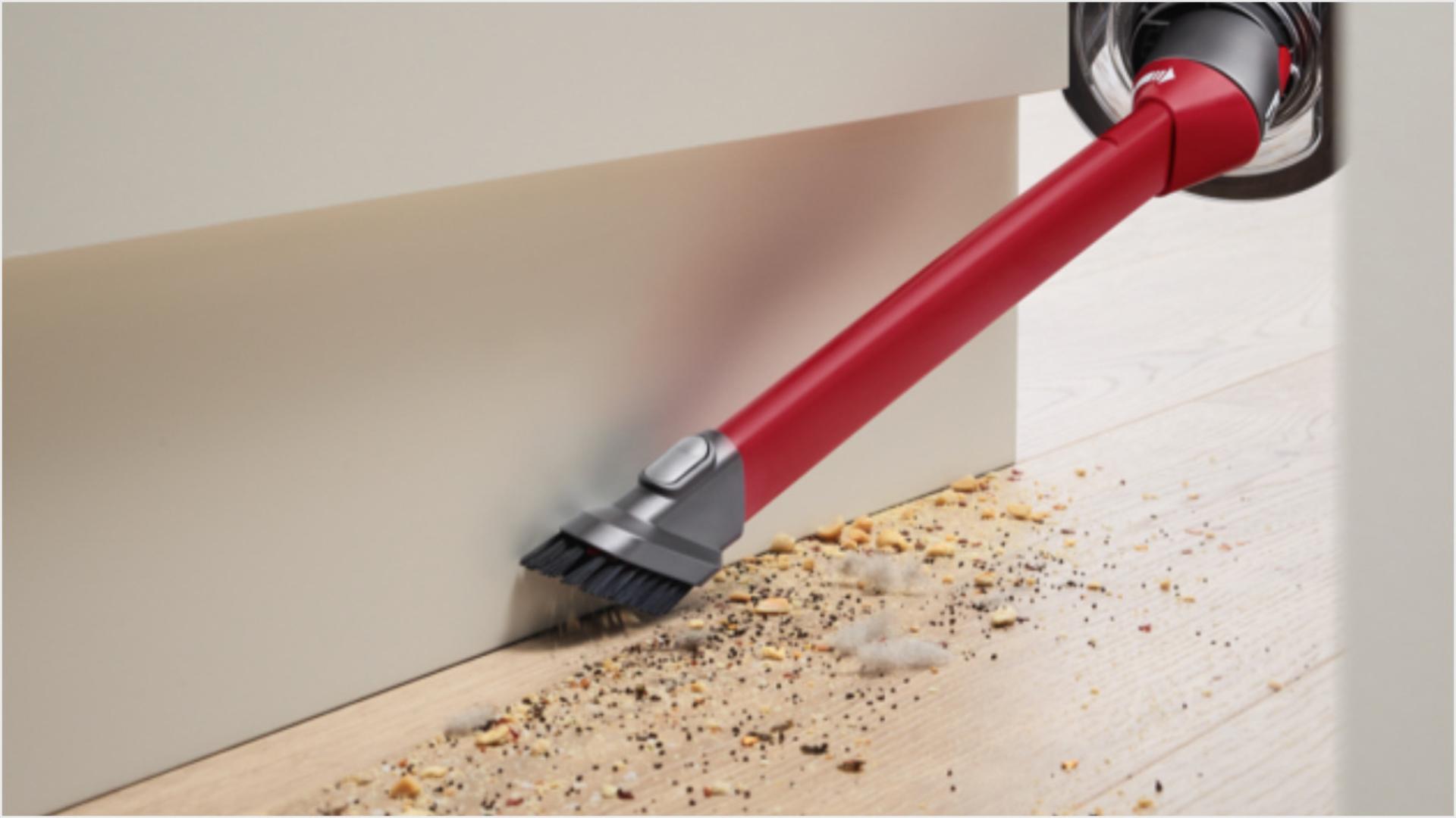 User cleaning floor around skirting board, with the Awkward gap tool attachment.
