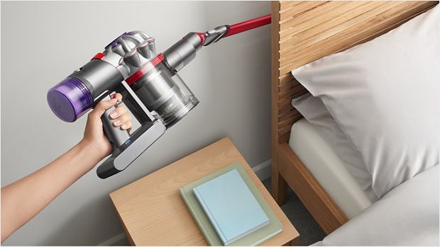User cleaning behind a bed headboard, with the Awkward gap tool attachment.