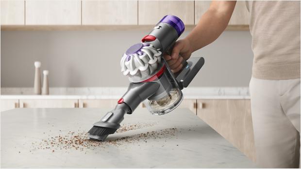 User cleaning crumbs from a kitchen countertop, with the Combination tool attachment.
