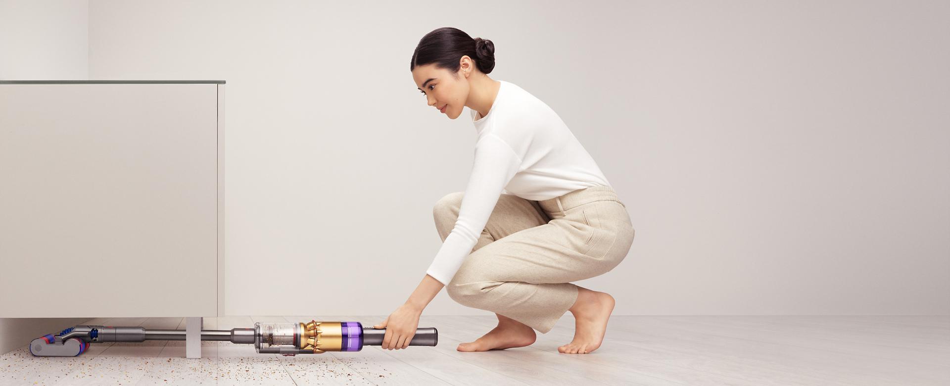 سيدة تَستخدم مكنسة Dyson Omni-glide™ للتنظيف أسفل خزانة.