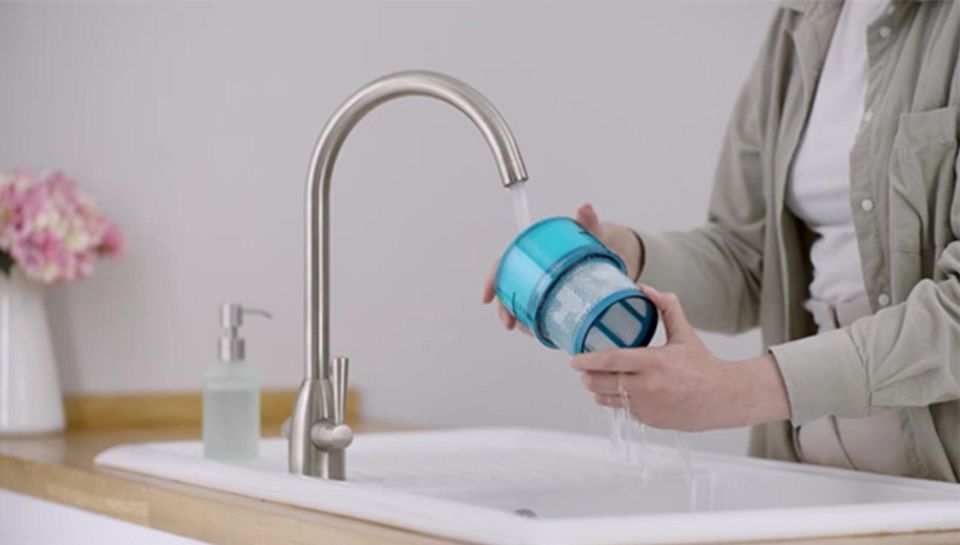 Osoba myjąca filtr HEPA odkurzacza pod bieżącą wodą