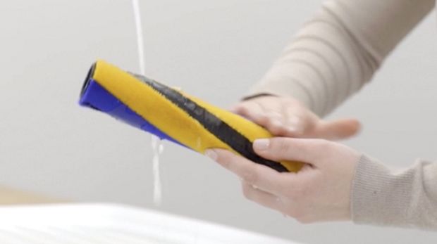 Par de manos sosteniendo la barra de cepillo lavable bajo el chorro de agua.