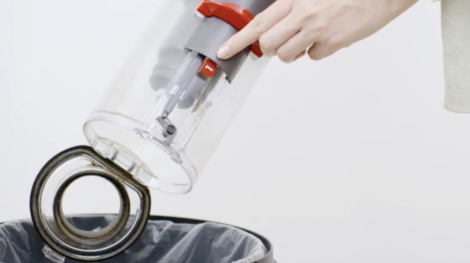 Hands cleaning out a transparent Dyson vacuum bin.