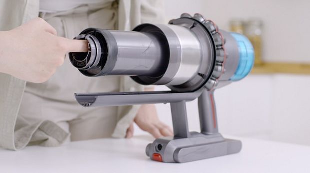 Mujer mostrando cómo despejar una aspiradora inalámbrica Dyson bloqueada.