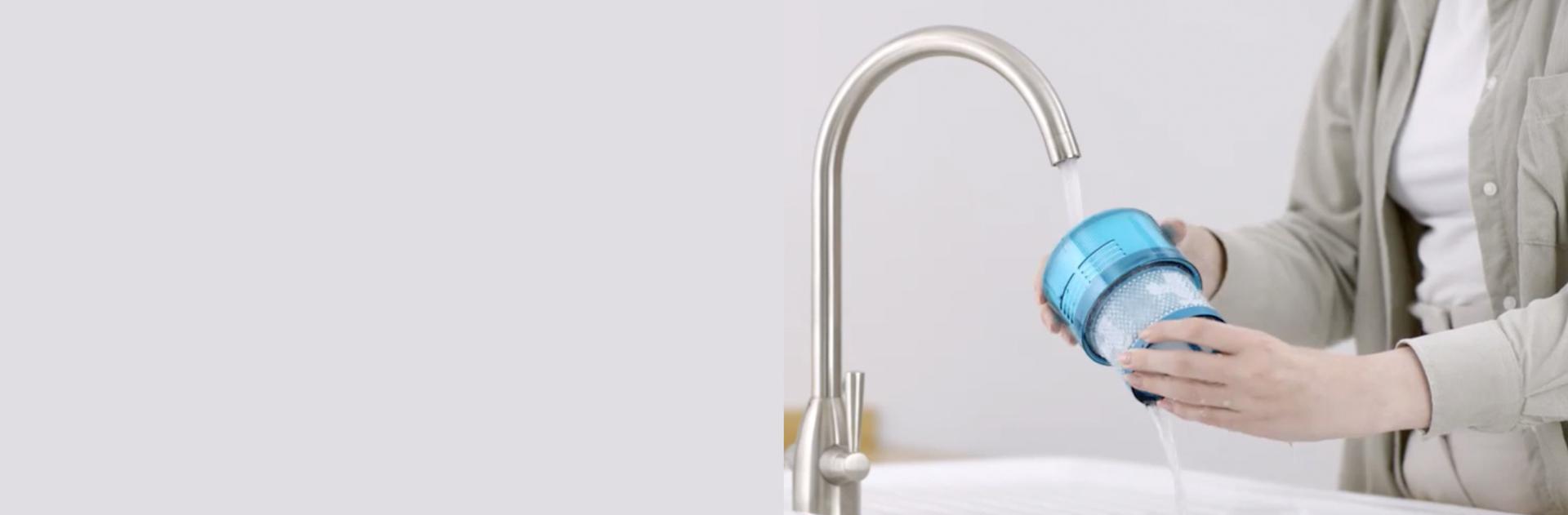 Hands holding a Dyson vacuum filter under a running water tap.