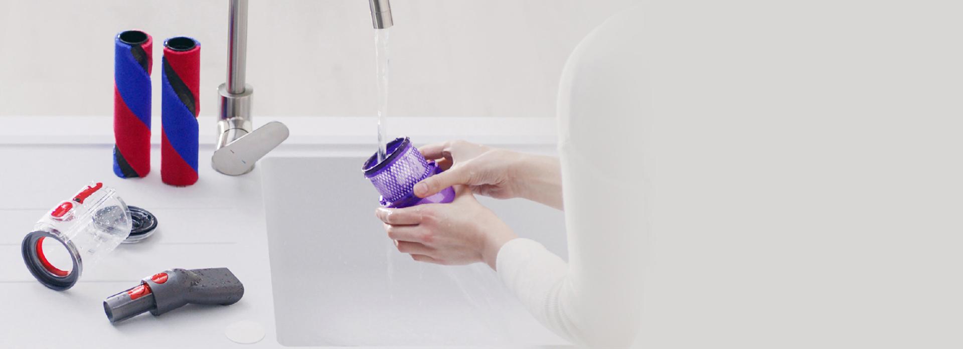 Brush bars, clear bin and worktop tool on a draining board while filter is being washed under running water.