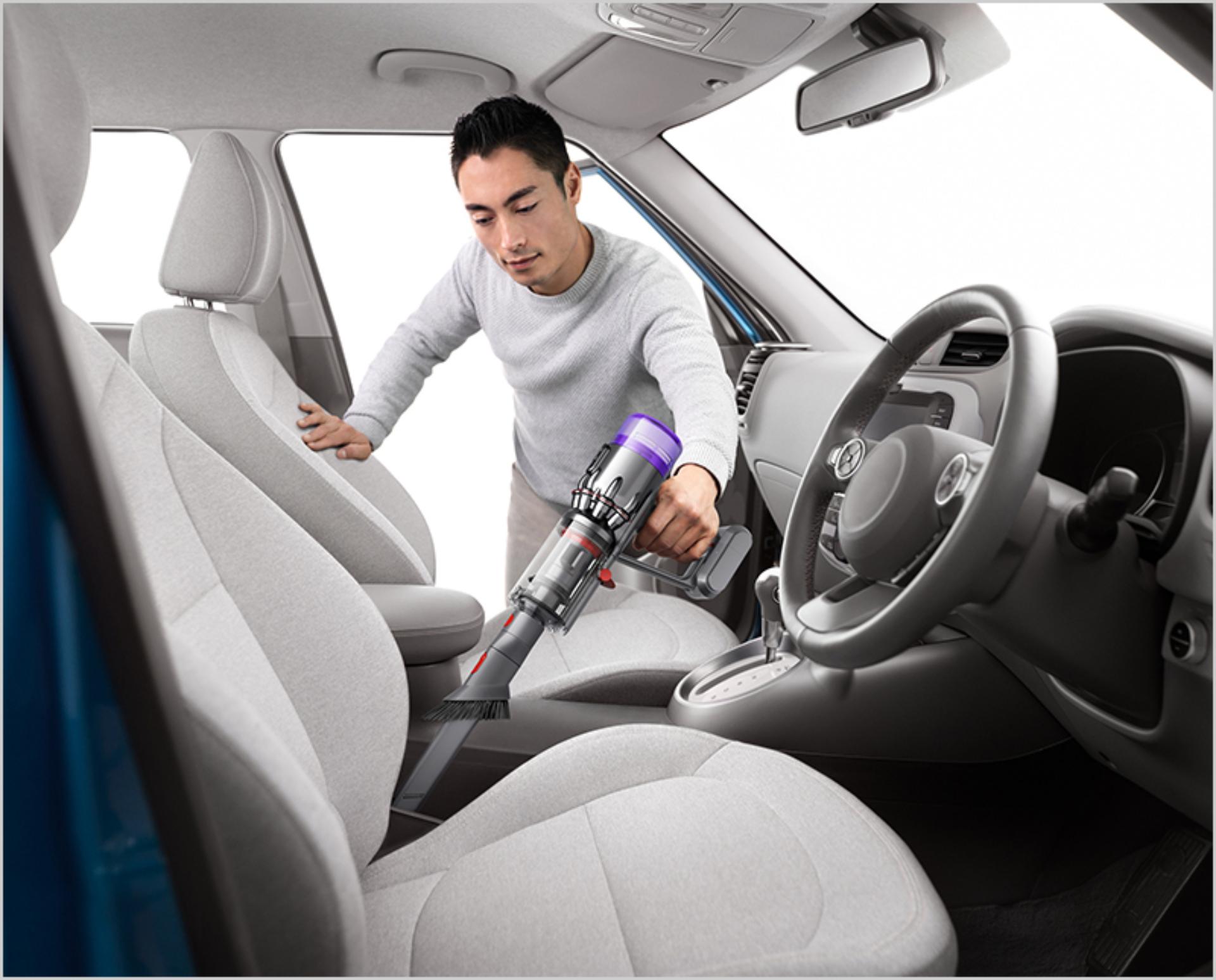 차 안을 청소하는 다이슨 마이크로 무선 청소기.