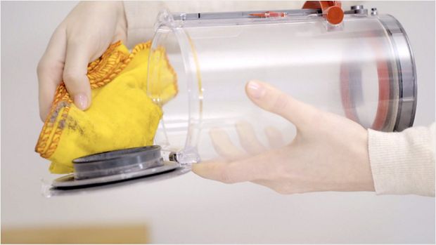 A user cleans the vacuum cleaner's bin with a duster.