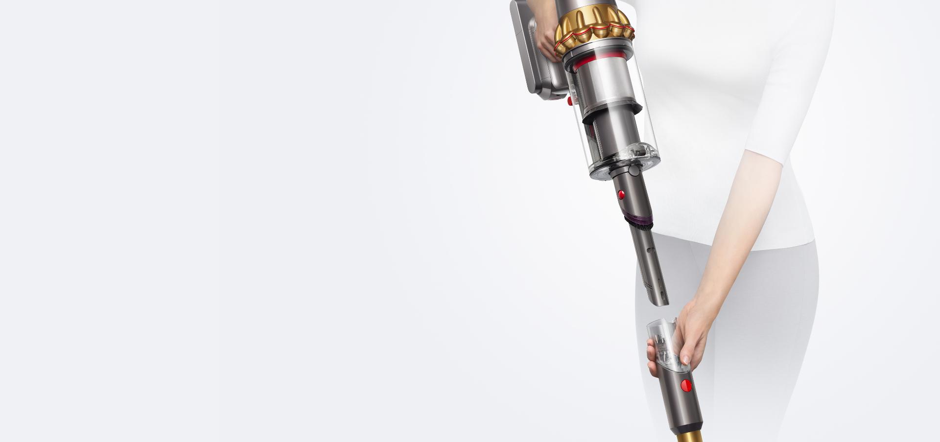 A woman holding the Dyson V15s main body high in one hand while removing the wand with the other revealing the ready-to-go crevice tool.