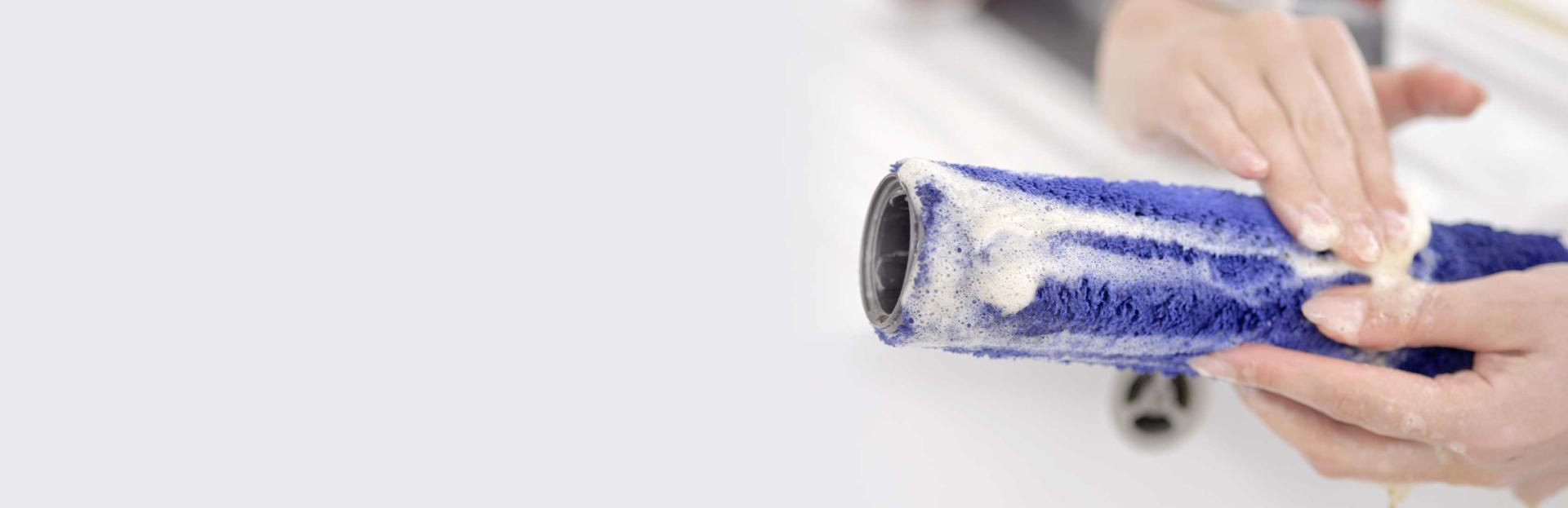 أيدي مستخدم بينما تغسل الرأس الأسطواني المُبلّل تحت الصنبور.