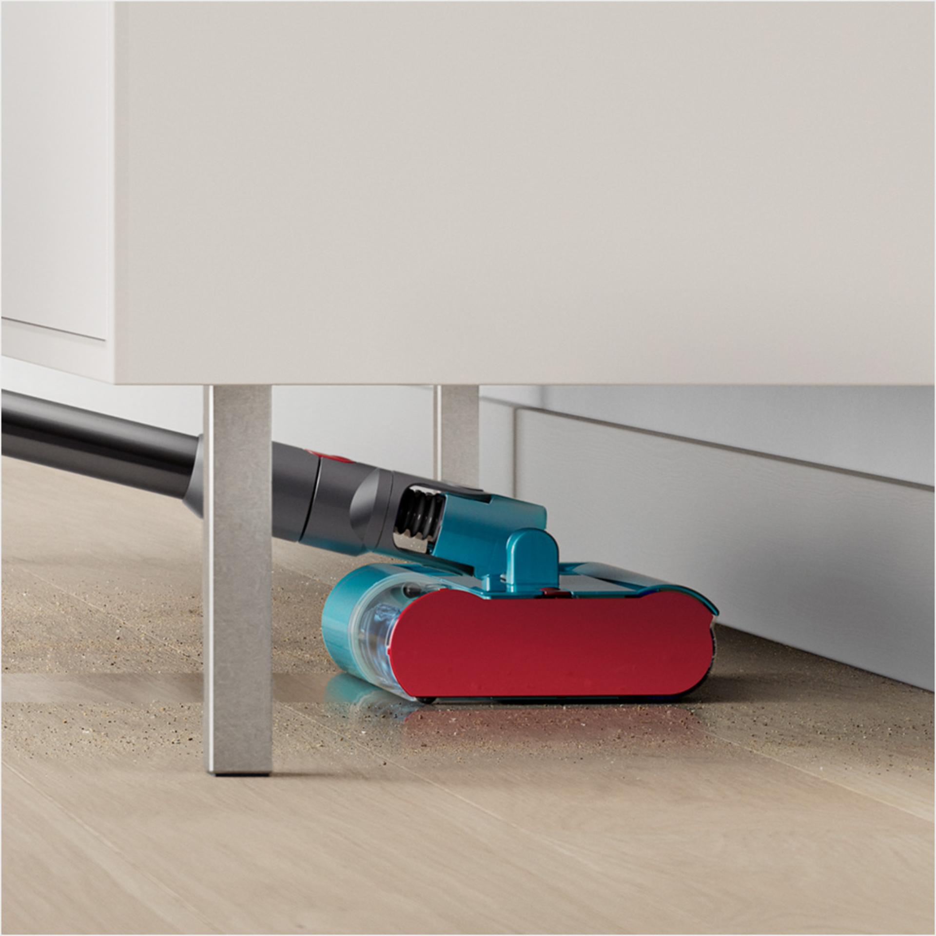 Dyson Submarine wet roller head reaching under a table as it cleans a hard floor.