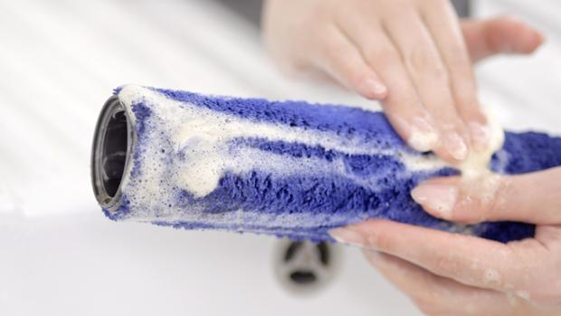 User's hands washing the wet roller cleaner head under a tap.