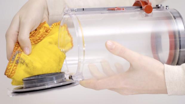 A user cleans the vacuum cleaner's bin with a duster.